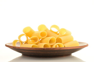 Bright yellow organic, uncooked pasta in a clay plate, close-up, isolated on white.