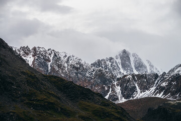 Atmospheric alpine landscape with great mountain peaked top with snow in low clouds. Dramatic mountain scenery with sharp pinnacle in overcast weather. Awesome view to snowy pointy peak in cloudy sky.