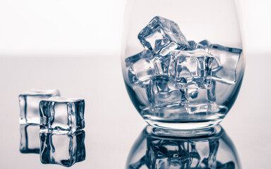 Ice cubes in a glass. Ice for soda or cocktails. Clear Frozen water. Ice maker. Fake or Artificial acrylic or plastic ice cubes on White background with reflection.  