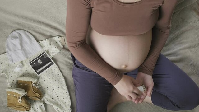 pregnant woman sitting on bed, pouring out pills from bottle on palm, top view