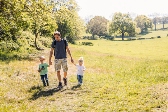Papa se balade main dans la main avec ses deux enfants à la campagne, dans les champs, en été. 