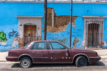 Broken down old car in front of weathered colourful building façade in the city of Oaxaca in Mexico