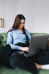 Naklejka premium Attractive pretty young woman using computer, sitting on comfortable sofa. Millennial woman sit at home and work on laptop. Home office concept
