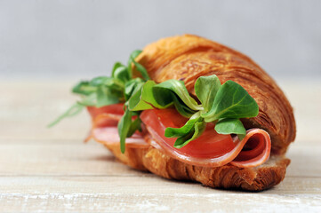 Croissant sandwich.  Sandwich filling with ham, tomato slices, arugula leaves and corn salad.  Wooden table surface.  Close-up.  Macro photography.