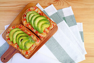 Top view of homemade grilled cheese toast with tomato and sliced avocado on wooden breadboard