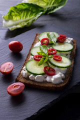 Fresh spring sandwich on a sliced gluten free sunflower bread. Red and green vegetables on black slate. Cucumber, chili and cottage cheese garnished with tomato and green leaves