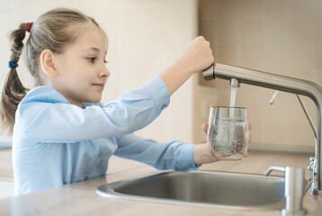Little child is drinking fresh and pure tap water from glass. Water being poured into glass from...