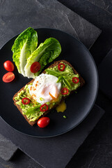 Fresh spring sandwich on a sliced gluten free sunflower bread. Red and green vegetables on black slate. Poached egg, avocado, chili and spring onion garnished with plum tomatoes