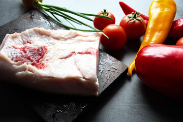 Raw chopped pork lard with meat on a wooden board with vegetables on a gray background for copy...