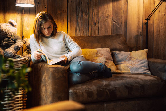 Jeune femme lit un livre sur son divan