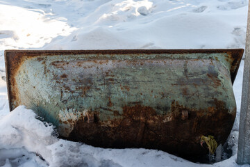 An old dilapidated cast-iron bathtub lies sideways in the snow. Scrap.