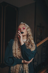 A blonde girl with a diadem in long hair and bright makeup posing on the stairs in the house.
