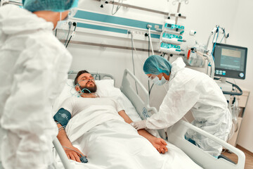 A doctor in a protective suit makes an injection into the vein of a patient suffering from coronavirus disease covid-19 in an intensive care unit. Treatment during a pandemic in a modern clinic.