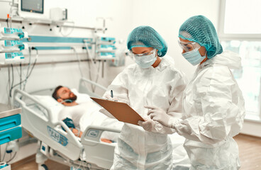 Doctors in protective suits check the card of a patient with coronavirus disease covid-19 in the intensive care unit. Treatment during a pandemic in a modern clinic.