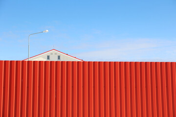 House behind a red fence against the blue sky