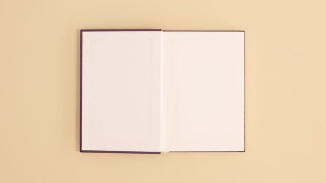 Purple hardcover vintage book appear and open with copy space on beige background. Stop motion flat lay
