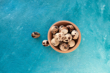 Small quail eggs in a light wooden small basket on a light yellow background in sunlight. Quail farm concept, keeping, breeding birds