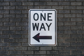 Closeup of a One Way Sign Posted on a Gray Brick Wall