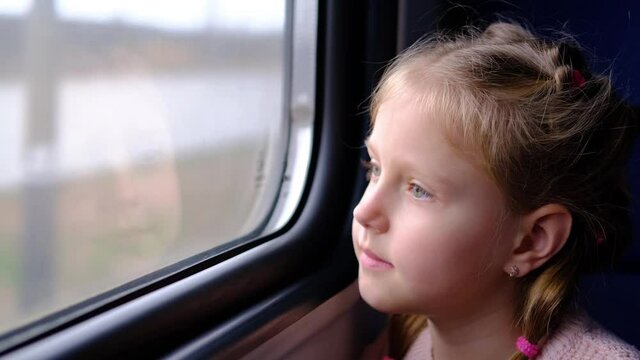 The child is on the train and looks out the window. A little girl travels in a train. 
