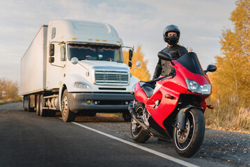 Motorbiker is standing on the countryside road on a truck background.