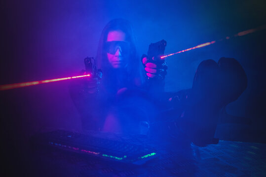 A girl with a toy guns is sitting in the smoke by the table with a computer keyboard above.