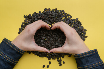 A pile of watermelon seeds on a yellow background in the shape of a heart