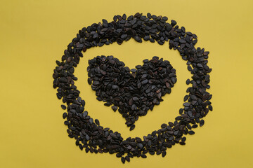 A pile of watermelon seeds on a yellow background in the shape of a heart