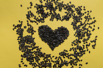 A pile of watermelon seeds on a yellow background in the shape of a heart