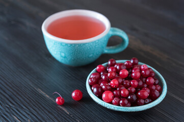 Small ceramic bowl full of fresh cranberry, turquoise ceramic cup with berry tea on the dark wooden background