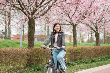 beautiful young woman of mixed races minority riding on bicycle in bloomy spring in casual clothes...