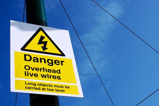 UK sign Danger. Overhead Live Wires against a blue cloudy sky.