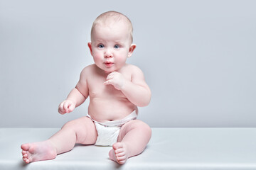 Funny sweet toddler boy sitting on white floor in diaper and looking with amazement isolated