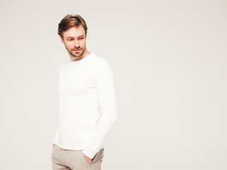 Portrait of handsome confident hipster lumbersexual businessman model wearing casual white sweater and trousers. Fashion stylish man posing against gray background in studio