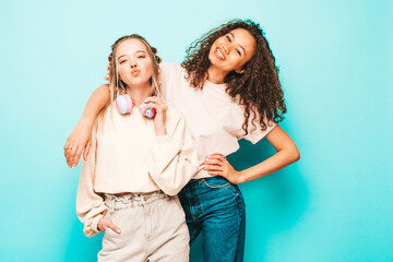 Two young beautiful smiling international hipster female in trendy summer clothes. Sexy carefree women posing near blue wall in studio. Positive models having fun. Concept of friendship