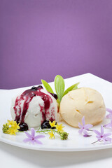 duas bolas de gelado num prato branco com flores comestíveis e doce de mirtilos