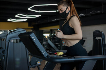 Fototapeta na wymiar Dedicated female athlete jogging on running track while wearing protective face mask in a gym during coronavirus epidemic.