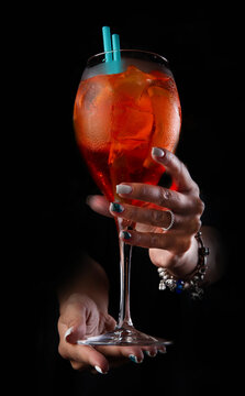Hands are holding a bright red cocktail. On a dark background. close-up.