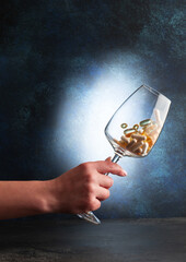 A hand holds a wine glass with various vitamins. Close-up.