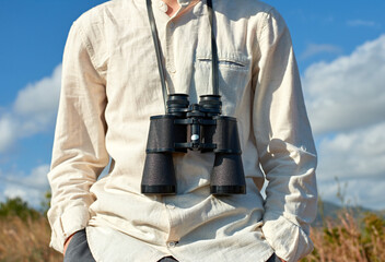 Closeup, front view of a relaxed young man in a white shirt with binoculars hanging around his neck