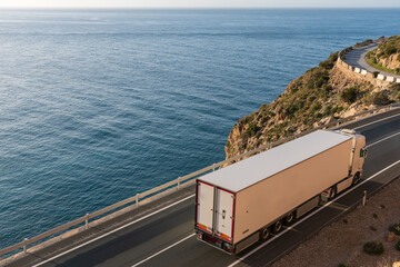 Truck with refrigerated semi-trailer driving on a road by the sea.