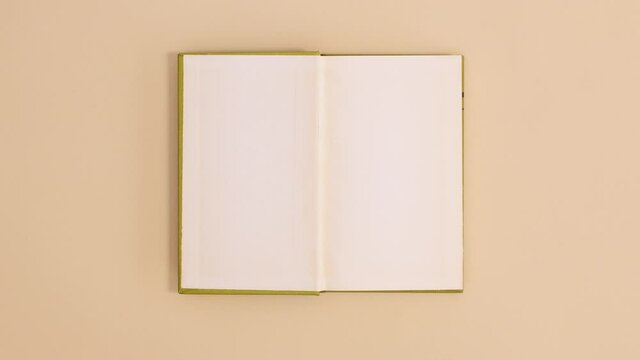 Bright green hardcover vintage book appear and open with copy space on beige background. Stop motion flat lay
