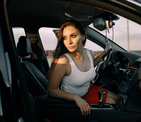 Fototapeta na wymiar Beautiful young girl driving a car in the evening in the sunset sun on an empty parking lot