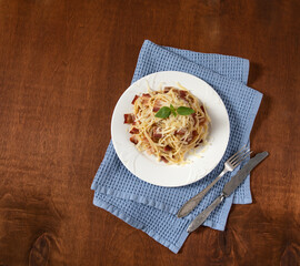 Spaghetti with bacon and parmesan cheese with basilic served on wooden background. Copy space.