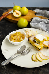 Sliced pie on a white plate with pear jam on a black table. Green pears in the background are blurred. Morning breakfast