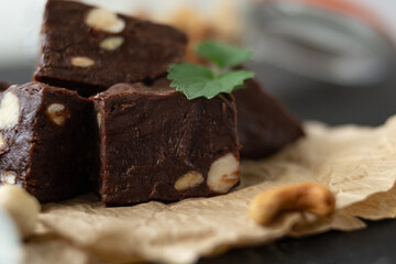 Homemade chocolate fudge garnished with mint leaves and served with tea on a black background. Nuts in the background blurred background. Copy space.