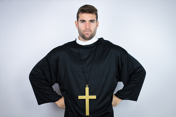 Young hispanic man wearing priest uniform standing over white background skeptic and nervous,...