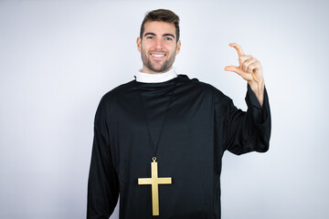 Young hispanic man wearing priest uniform standing over white background smiling and confident...