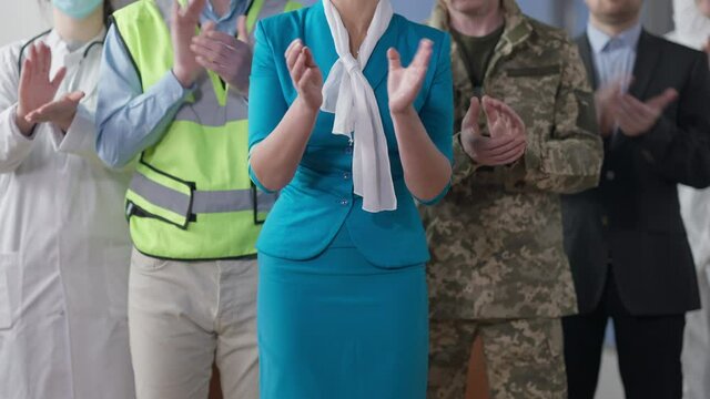 Unrecognizable Caucasian stewardess, soldier, builder, doctor and businessman clapping. Group of happy people of different professions standing indoors. Occupation and diversity