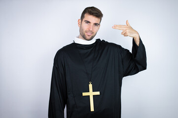 Young hispanic man wearing priest uniform standing over white background Shooting and killing...