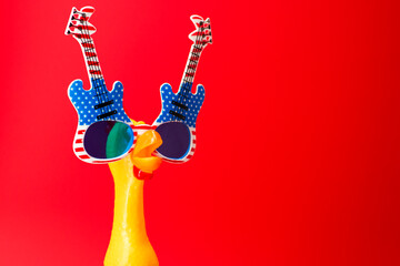 Screaming chicken toy in glasses on a red background. Yellow chicken toy in colorful glasses with...